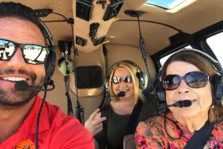 Three people smiling inside a helicopter, wearing headsets.