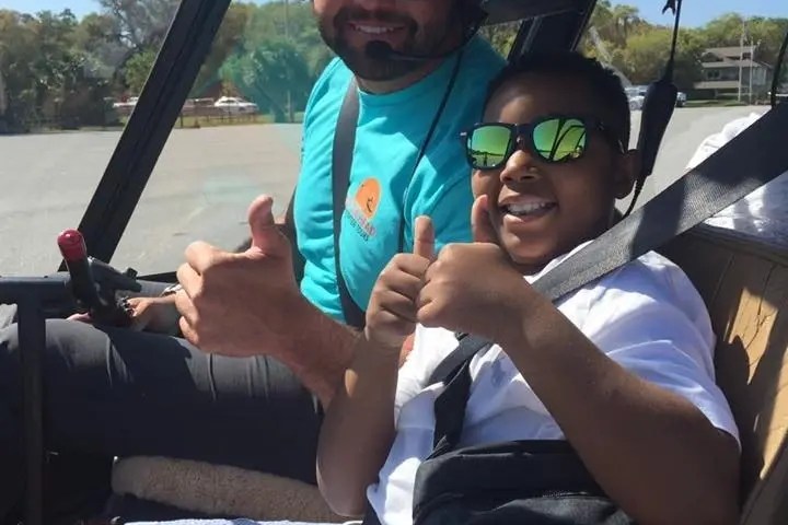 Two people in a helicopter giving thumbs up, both wearing sunglasses and headsets.