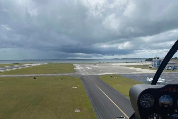 View from aircraft cockpit of runway and stormy clouds over the sea.