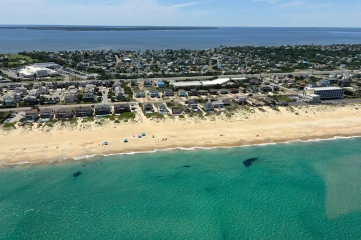 Aerial view of a beach with clear water, sandy shore, and adjacent coastal town.